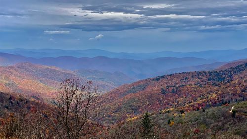 A panoramic view of colorful autumn mountains under a cloudy sky, showcasing vibrant foliage in the valleys.