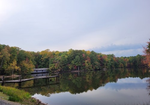 A serene lake surrounded by colorful autumn trees, with a wooden dock extending into the calm water.