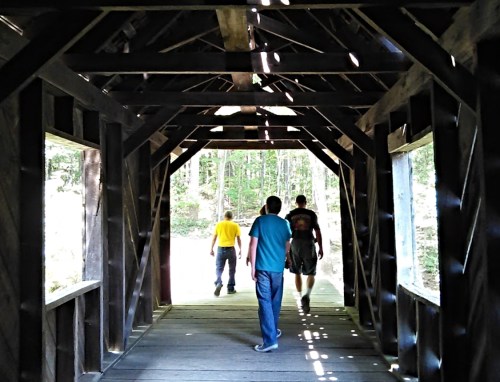 Three people walking through a wooden bridge with sunlight streaming through the gaps in the structure.