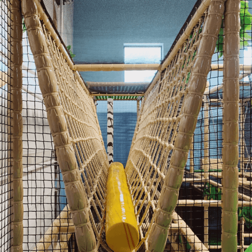 A colorful indoor play structure featuring netting and a yellow tube for children to crawl through.