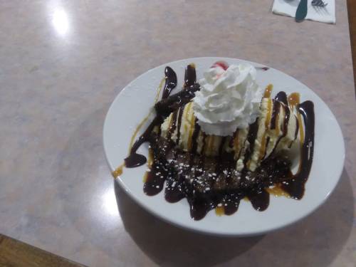 A dessert plate featuring a chocolate brownie topped with ice cream, whipped cream, and drizzled with chocolate and caramel sauce.
