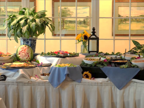 A beautifully arranged buffet table with various dishes, garnished with flowers and greenery, set in a bright room.