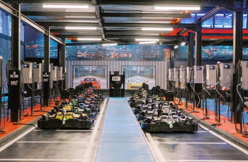 A go-kart track with multiple karts lined up, surrounded by charging stations and a city skyline backdrop.