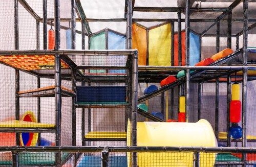 Colorful indoor playground structure with slides, tunnels, and climbing areas, enclosed by safety netting.