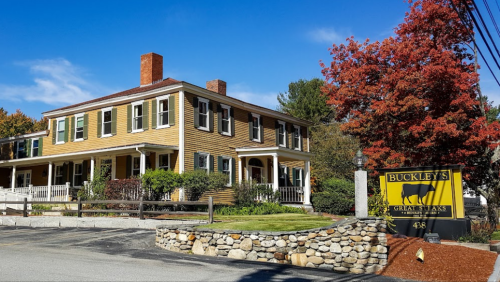 A charming yellow house with green shutters, surrounded by trees, and a sign for Buckley's Great Steaks.