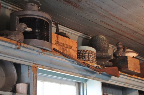 A rustic shelf displaying various vintage items, including a duck decoy, wooden boxes, and an old rifle.