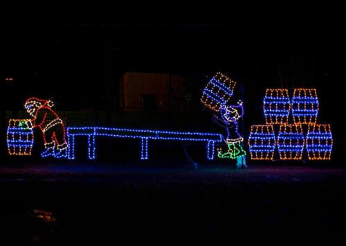 Colorful holiday lights depict two figures, one lifting a barrel and the other working at a table, against a dark background.