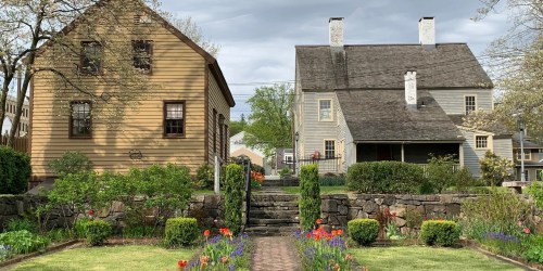 Two charming houses with gardens and stone pathways, surrounded by colorful flowers under a cloudy sky.