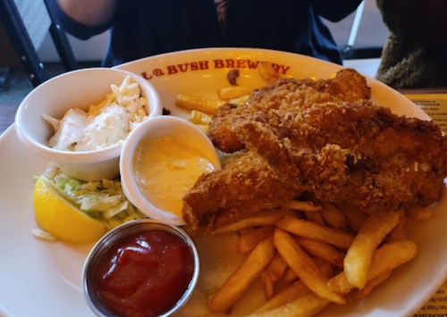 A plate of fried fish fillets with fries, coleslaw, lemon, and dipping sauces at a restaurant.