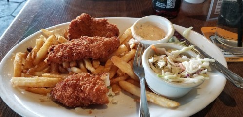A plate of crispy fried fish fillets served with French fries, coleslaw, and dipping sauce.