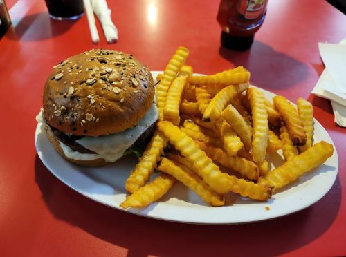 A plate with a sesame seed bun burger and a generous serving of crinkle-cut fries on a red table.