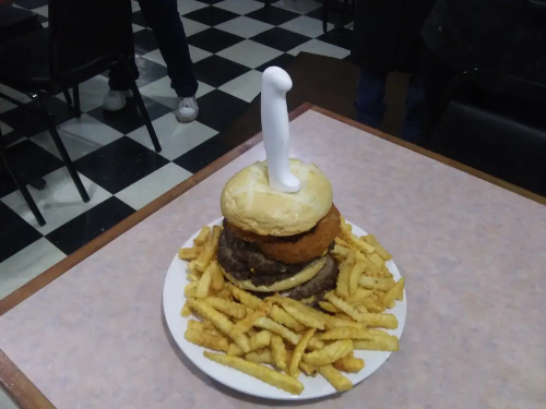 A large burger with a chicken patty and fries, topped with a white object resembling a novelty item.