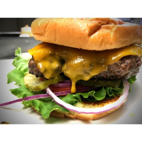 Close-up of a cheeseburger with melted cheddar, lettuce, pickles, and red onion on a toasted bun.