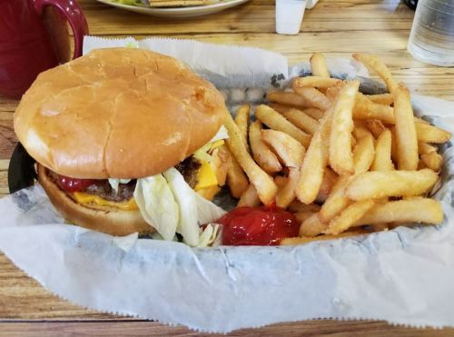 A cheeseburger with lettuce on a bun, served with a side of crispy fries and ketchup on a paper-lined plate.