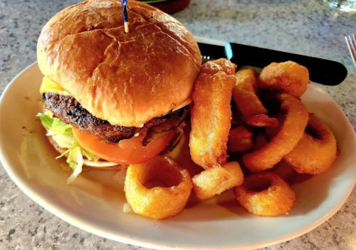 A juicy burger with lettuce and tomato, served with a side of crispy onion rings on a plate.