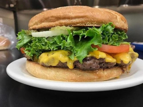 A delicious cheeseburger with lettuce, tomato, pickles, and melted cheese on a toasted bun, served on a plate.