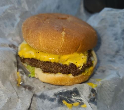 A cheeseburger with a melted cheese slice, lettuce, and a toasted bun, wrapped in paper.