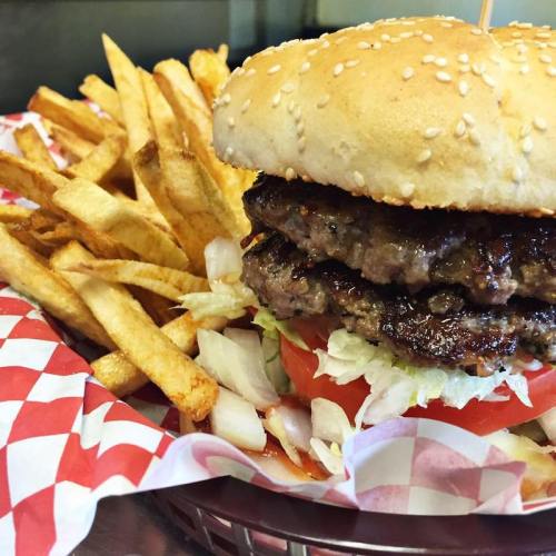 A juicy double burger with lettuce, tomato, and a sesame seed bun, served with a side of crispy French fries.