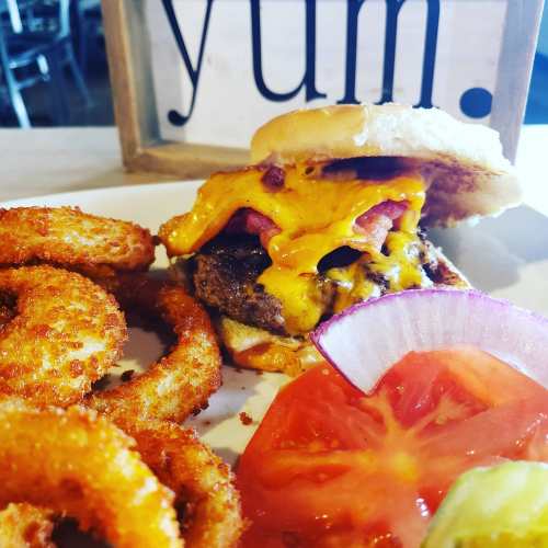 A juicy cheeseburger with melted cheese, topped with tomatoes, served with crispy onion rings and fresh tomato slices.