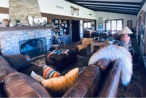 Cozy living room with a stone fireplace, leather sofas, colorful cushions, and wooden furniture. Warm and inviting atmosphere.