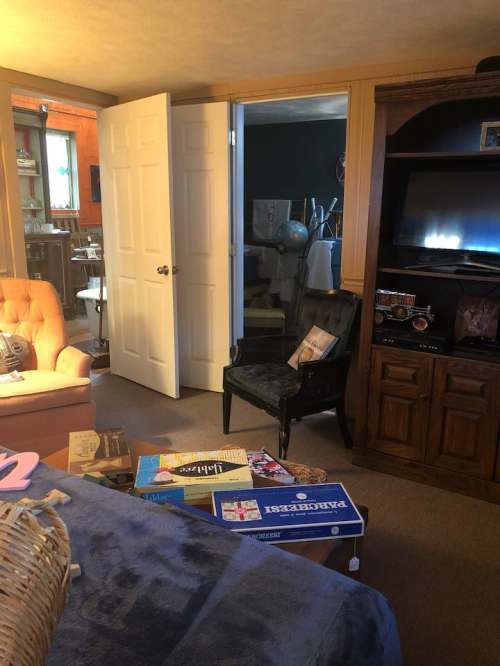 Cozy living room with a peach sofa, a black chair, and a coffee table cluttered with board games and books.