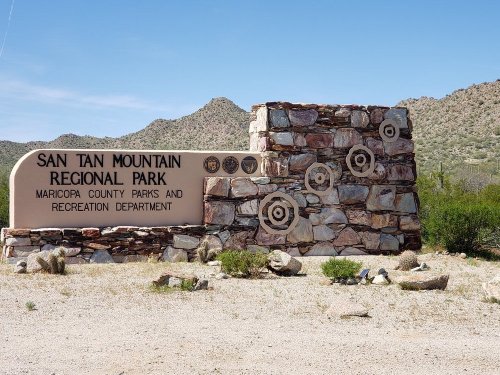 Sign for San Tan Mountain Regional Park, featuring stone structure and desert landscape in the background.