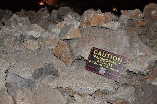 A caution sign on rocky terrain warns of recorded paranormal activity in the area.