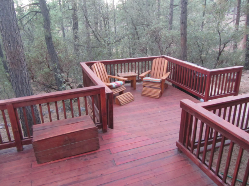 A wooden deck surrounded by trees, featuring two chairs and a storage box.