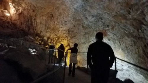 A group of people walking along a lit path inside a cave, surrounded by rocky walls and dim lighting.