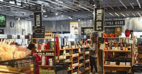 A bustling store filled with shelves of olive oils, vinegars, and wines, with shoppers browsing the aisles.
