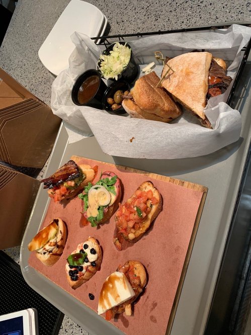 A platter with various small sandwiches and bruschetta topped with tomatoes, olives, and sauces on a wooden board.