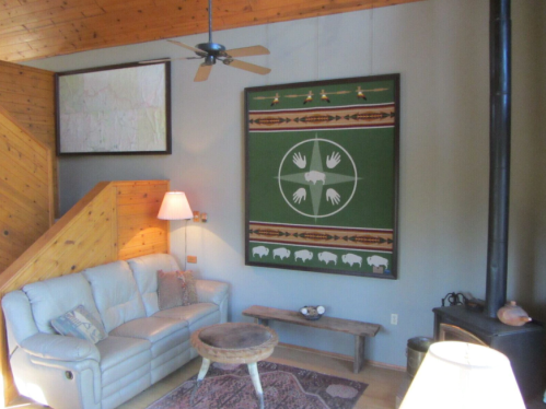 Cozy living room with a white sofa, wooden coffee table, and a large green wall hanging featuring hands and buffalo.