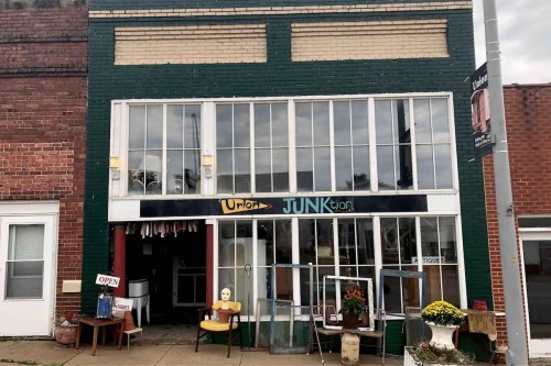 A green and brick storefront with large windows, displaying various items and a sign that reads "Union JUNKtion."