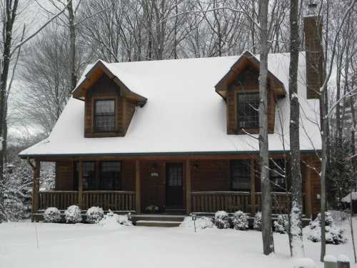 A cozy wooden cabin covered in snow, surrounded by trees in a winter landscape.