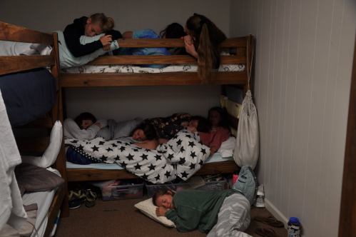 A cozy room with children sleeping on bunk beds and the floor, wrapped in blankets, creating a peaceful atmosphere.