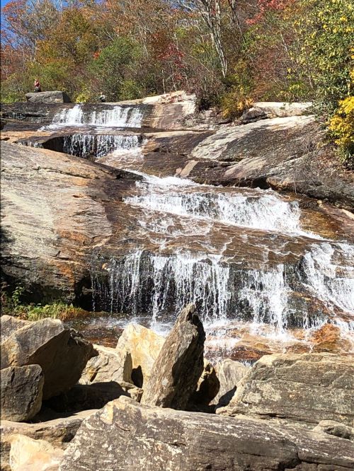 A serene waterfall cascades over rocky terrain, surrounded by colorful autumn foliage.
