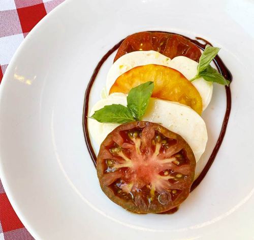 A plate with layered slices of colorful tomatoes and mozzarella, garnished with fresh basil and a drizzle of balsamic.