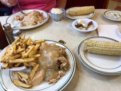 A table set with two plates of turkey with gravy, fries, and corn on the cob, plus a small dish of coleslaw.