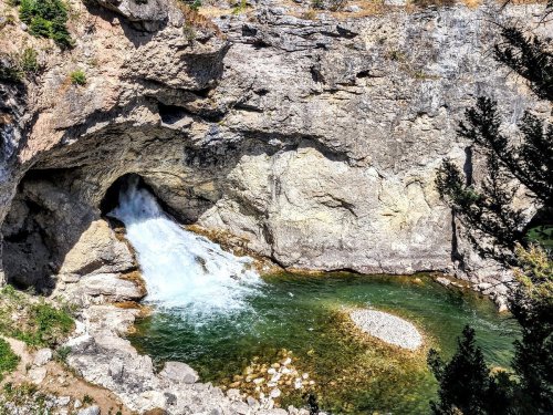 A waterfall cascades into a clear pool surrounded by rocky cliffs and greenery.