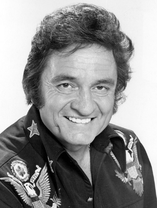 Black and white portrait of a smiling man with dark, wavy hair, wearing a decorative shirt with eagle motifs.