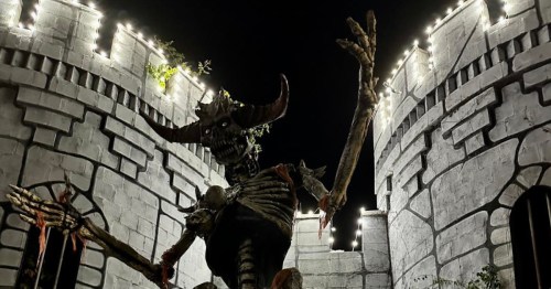 a night shot of the exterior of the Castle of Muskogee with its turrets adorned with lights and a demonic figure lurking over everyone who dares to enter the castle during the halloween festiva