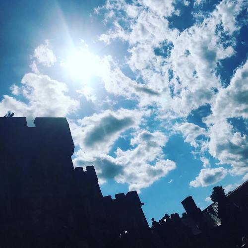 Silhouette of a castle against a bright blue sky with fluffy clouds and sunlight shining through.