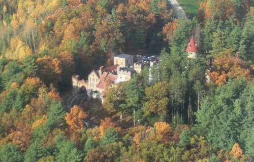 Aerial view of a castle surrounded by vibrant autumn foliage and green trees.