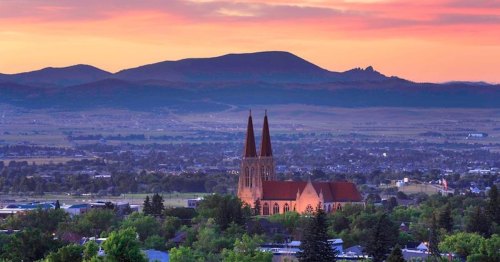 A scenic view of a church with spires at sunset, surrounded by mountains and a valley landscape.