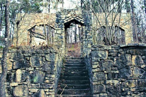 Stone ruins with archways and stairs, surrounded by overgrown trees and vegetation.