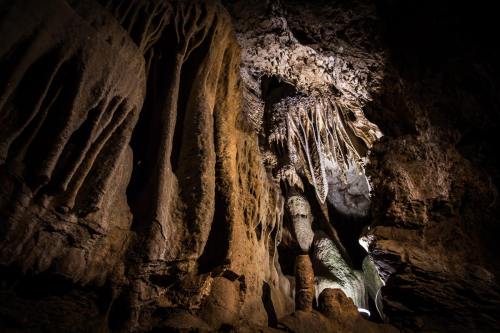 Stalactites and rock formations illuminated in a dark cave, showcasing intricate textures and shadows.