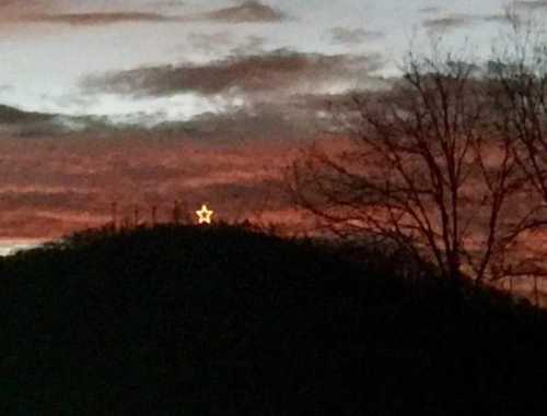 A glowing star atop a hill against a colorful sunset sky, with silhouetted trees in the foreground.