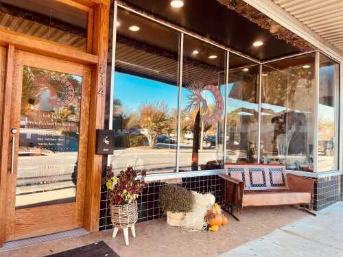 A storefront with large windows, a wooden door, and a bench adorned with autumn decorations and plants.