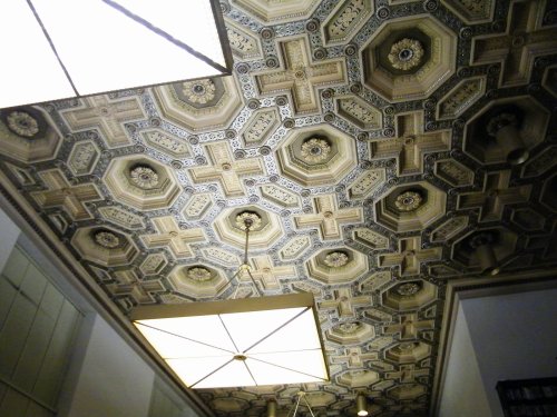 Ornate ceiling with intricate geometric patterns and decorative details, illuminated by modern light fixtures.