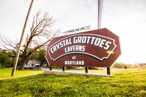 Sign for Crystal Grottoes Caverns of Maryland, set against a grassy landscape and clear sky.